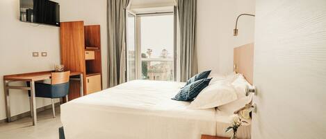 A hotel room with a bed, a desk, a TV, and a view of the outside.