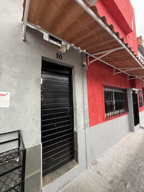 Um edifício com uma porta de persiana preta fechada, o número '10' em destaque acima e fachada vermelha e cinza.