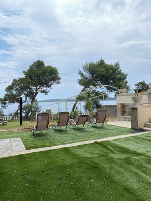 A patio with artificial grass, three lounge chairs, and a pergola overlooking a body of water. - Uz obalu mora, luksuzna villa sa jacuzzyjem, (Hvar)