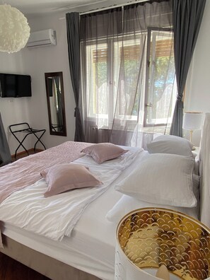 A neatly made bed with pillows, a bedside lamp, a television on the wall, and a window with curtains. - Uz obalu mora, luksuzna villa sa jacuzzyjem, (Hvar)