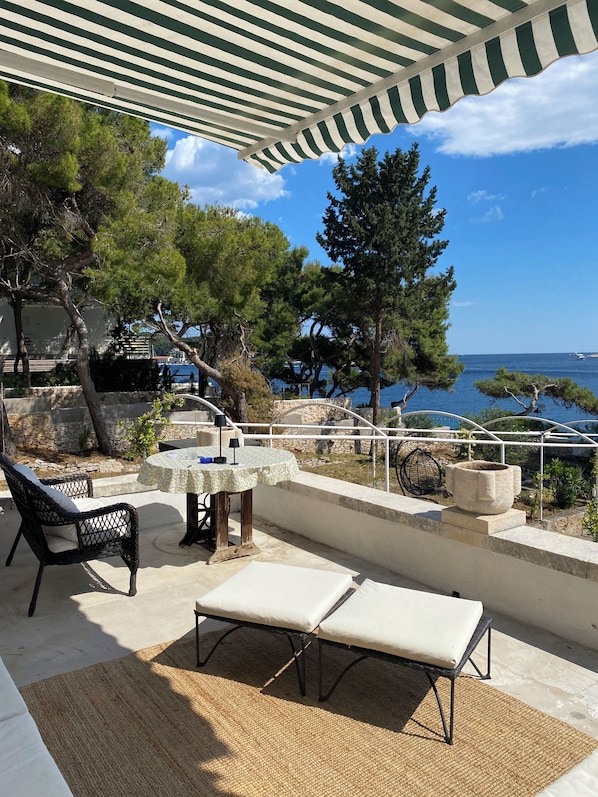 A terrace with a table and chairs, overlooking a body of water and a stone wall. - Uz obalu mora, luksuzna villa sa jacuzzyjem, (Hvar)
