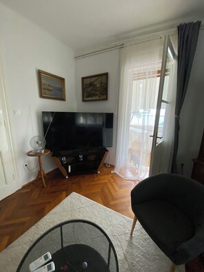 A living room with a flat-screen TV, a wooden floor, a chair, and a window with curtains. - Uz obalu mora, luksuzna villa sa jacuzzyjem, (Hvar)