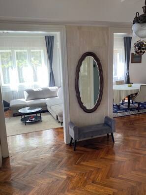 Ein Wohnzimmer mit einer Couch, einem runden Couchtisch, einer Bank, einem großen Spiegel und einem Essbereich mit Tisch und Stühlen.