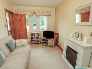Una sala de estar con sofá, televisión, estantería, chimenea y ventana con cortinas.