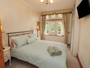 A bedroom with a bed, nightstands, a lamp, a window with curtains, and a TV mounted on the wall. - The Haven (Morecambe)