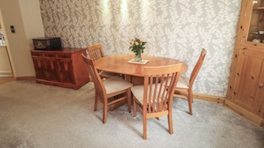 Uma área de refeições com uma mesa e cadeiras de madeira, um vaso com flores, um armário de madeira e piso coberto de carpete.