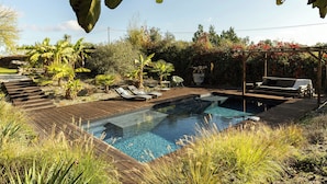 Une piscine entourée d’une terrasse en bois, de chaises longues et de plantes tropicales.