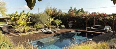 Una piscina con cubierta de madera, sillas de descanso y plantas tropicales.