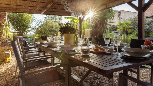 Un espace de restauration en plein air avec une table en bois, des chaises et un luminaire suspendu.