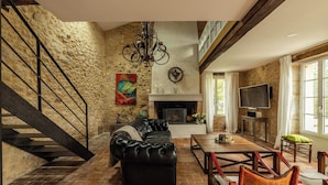 Un salon spacieux avec une cheminée, un canapé en cuir noir, une table à manger et un escalier.