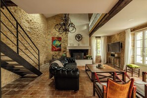 Ein geräumiges Wohnzimmer mit Kamin, einer schwarzen Ledersofa, einem Esstisch und einer Treppe.
