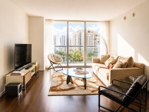 Ein modernes Wohnzimmer mit Fernseher, einer Couch, Sesseln und einem großen Fenster mit Blick auf die Stadt.