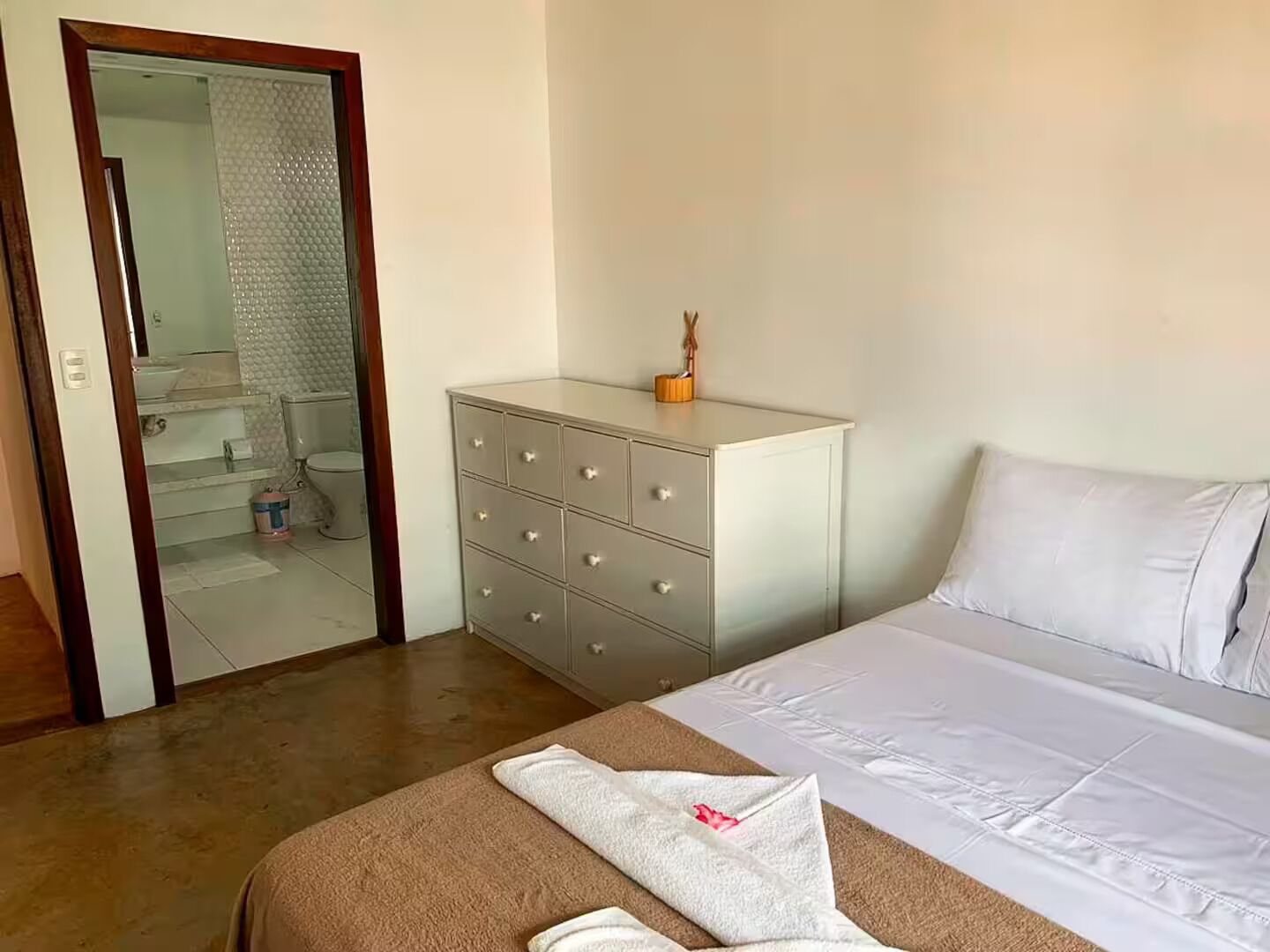 Hotelkamer met een bed, een dressoir, een zichtbare badkamer door een glazen deur en een vloerbedekking.