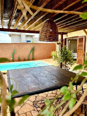 A poolside area with a table, a hanging light fixture, and a view of a building in the background.