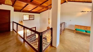 A spacious interior with a wooden ceiling, a balcony with a wooden railing, and a green cushioned bench.