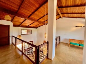 A spacious interior with a wooden ceiling, a balcony with a wooden railing, and a green cushioned bench.