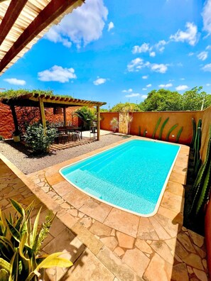 A swimming pool with a stone deck, surrounded by cacti and a pergola.