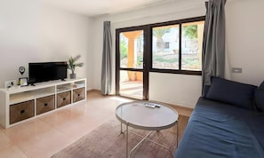 A modern living room with a flat-screen TV, a sofa, a small round table, and a sliding glass door leading to an outdoor area. - Oasis Dunas Eguzkilore Sun & Pool by B-Rent: Your Ideal Retreat in Corralejo (Corralejo)