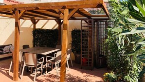 A wooden pergola with a table and chairs, surrounded by potted plants and a garden. - San Frediano, terrace, patio, and heating pool (Firenze)