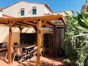 Una pérgola de madera con una mesa y sillas, rodeada de plantas en macetas y un jardín.