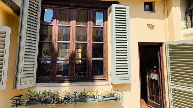 A building with a large window with shutters, a small door, and a balcony with potted plants. - San Frediano, terrace, patio, and heating pool (Firenze)