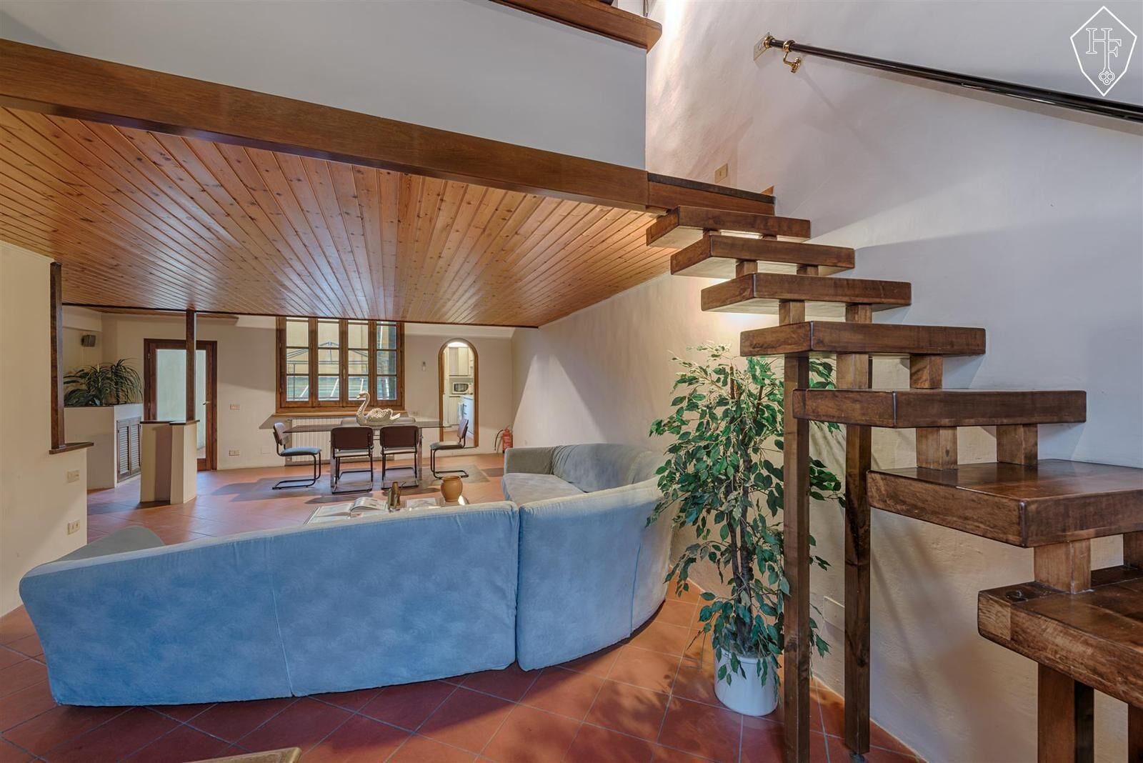 Um interior moderno com um sofá azul curvo, escada de madeira e uma planta em vaso.