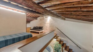 A loft-style bedroom with exposed wooden beams, a bed, a bench, and a staircase. - San Frediano, terrace, patio, and heating pool (Firenze)
