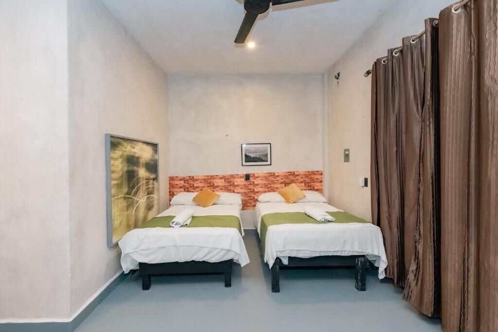 Una stanza con due letti, un ventilatore a soffitto, una parete decorata in mattoni e un'ampia finestra.