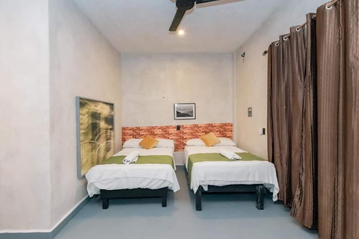 A room with two beds, a ceiling fan, a brick accent wall, and a large window.