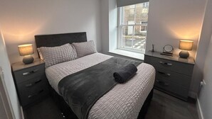 Ett modernt sovrum med en stor säng, sängbord, ett fönster med utsikt och en liten byrå.