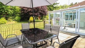 Une terrasse extérieure avec une table et des chaises, un grand parasol et un espace clos par des parois de verre, également équipé de chaises.
