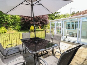 An outdoor patio with a table and chairs, a large umbrella, and a glass-enclosed area with chairs. - 51 Colin Mclean Road (Dereham)