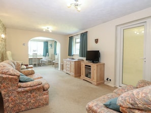 A living room with floral-patterned sofas, a television on a wooden cabinet, and a dining area with chairs and a table. - 51 Colin Mclean Road (Dereham)