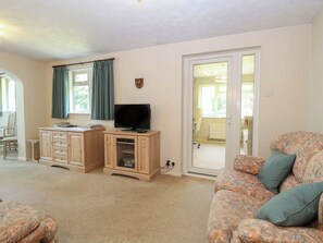 A living room with a television on a wooden cabinet, a patterned sofa, and a door leading to another room. - 51 Colin Mclean Road (Dereham)