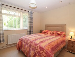 A bedroom with a bed, a radiator, a window with curtains, a bedside lamp, and a wooden nightstand. - 51 Colin Mclean Road (Dereham)