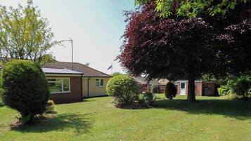A residential property with a well-maintained lawn, a small tree, and a brick building with a tiled roof.