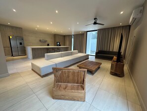 Um espaço de estar moderno com cozinha, sofá, mesa de centro de madeira e aparador para TV.