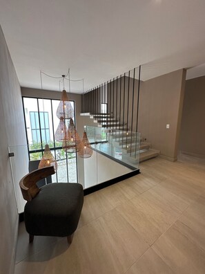Um interior moderno com escada, guarda-corpo de vidro e luminária pendente.