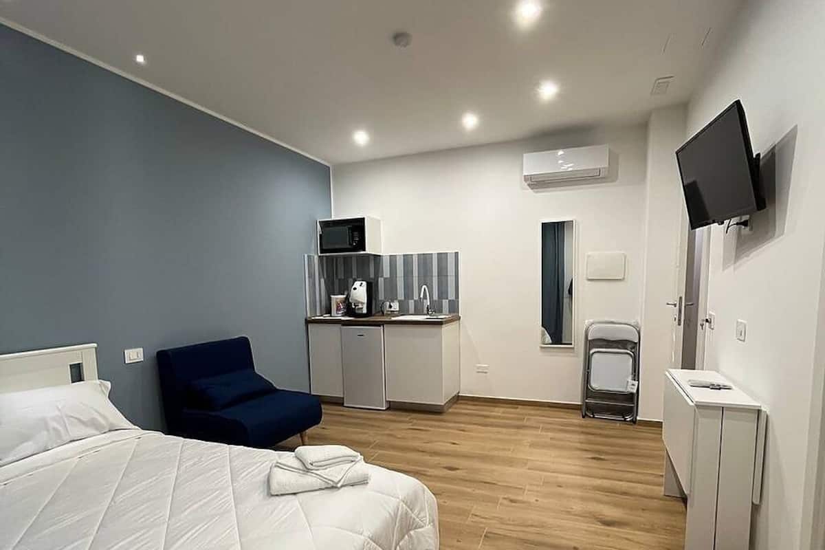 Una habitación de hotel moderna con una cama grande, zona de estar, kitchenette, televisor y baño.