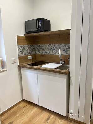 Cocina compacta con microondas, pileta y protector de pared de madera.