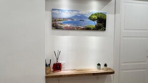 A modern interior with a wooden shelf, a painting of a coastal landscape, and a white door. - The Family Rooms (Naples)