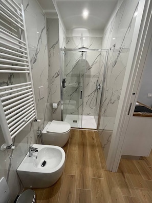 A bathroom with a bidet, toilet, and glass-enclosed shower. - The Family Rooms (Naples)
