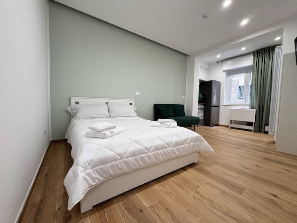 A modern hotel room with a large bed, a green armchair, and a view of the city. - The Family Rooms (Naples)