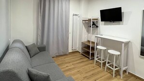 A modern living room with a grey sofa, a white TV mounted on the wall, and a wooden floor. - The Family Rooms (Naples)