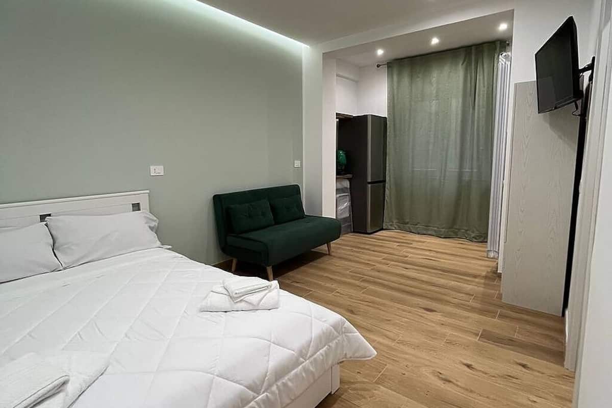 Una habitación de hotel con una cama, un sofá verde, un televisor de pantalla plana y suelo de madera.