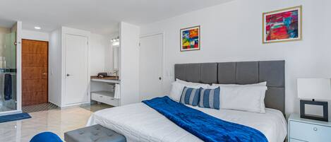 A modern bedroom with a large bed, a grey headboard, a bedside table with a lamp, and a blue bench.