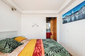 Un dormitorio con cama, perchero, un cuadro en la pared y vista a otra habitación.