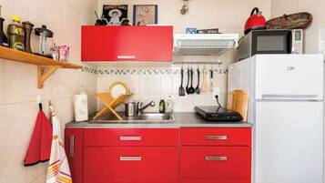 A kitchen with red cabinets, a white refrigerator, a microwave, and various kitchen utensils.