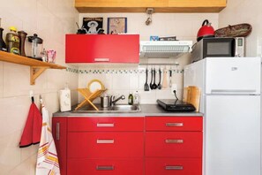 Een keuken met rode kastjes, een witte koelkast, een magnetron en diverse keukengerei.