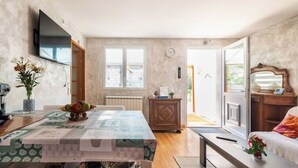 A dining area with a table, chairs, a clock, and a view through a glass door. - A39, Exit N*5, T1: Quiet/Peaceful/Relaxing/Safe. Sleeps 2 (140/200) + pets (Tréclun)